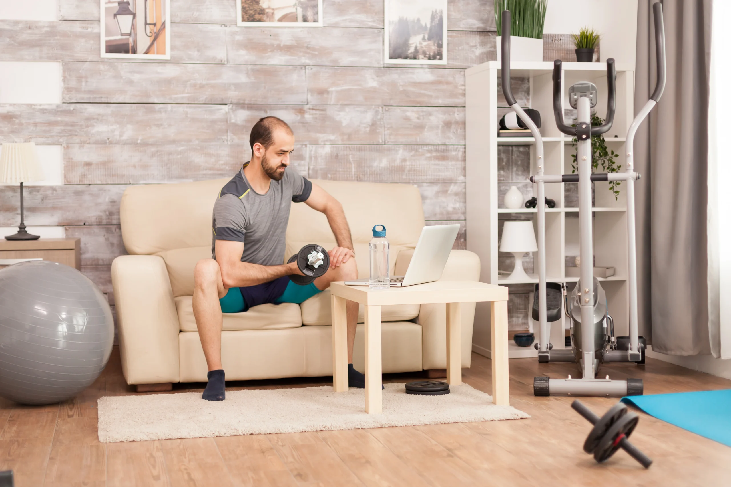 fit-man-sofa-training-biceps-with-dumbbell-watching-online-workout-time-self-isolation