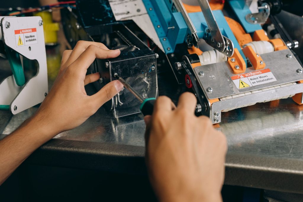 Hands of a technician repairing robotic machinery with precision tools on a workbench.